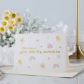 Tarjeta de felicitación plegable blanca con texto dorado "you are my sunshine" e iconos. - Eres mi Sol