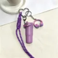 Paarse mini beker waterfles sleutelhanger detail met geweven koord en hoofdtelefoon. - Paars
