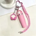 Detailopname van roze mini waterfles en koptelefoon sleutelhanger met gevlochten koord voor tas. - Roze