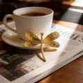 Vue détaillée d'une broche libellule en acier inoxydable doré posée contre une tasse - Libellule Dorée à la Mode (CXXZ009-B)