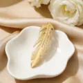 Elegant gold feather brooch with shimmering crystals on white floral ceramic display - Left Feather (CXXZ019-zuo)