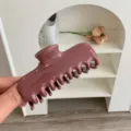 Primer plano de una pinza para el pelo de PC color malva brillante sujeta con la mano - Rojo Oscuro