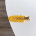 Detail view of a stylish yellow polka dot non-marking hair clip with a gold metal base. - Yellow