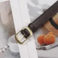 Primo piano della cintura in pelle marrone scuro con fibbia dorata su sfondo estetico. - Fibbia Dorata Caffè