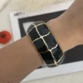 Vista dettagliata di un ampio bracciale rigido dorato con motivo a griglia nera. - Stile Plaid Geometrico (3556) / nero e oro