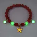 Macro detail showing the glowing effect of a luminous starfish charm beaded bracelet. - Bracelet / Gold (Red Turq Orange)
