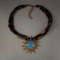 Close-up detail of a glowing blue sun pendant on a chic leopard print fabric cord necklace - Gold Blue Glow Necklace