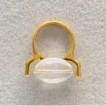 Gedetailleerde opname van een vergulde messing ring met een helder ovaal glaselement. - Goud