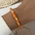 Detail view of orange enamel floral bangle with gold leaf patterns in vintage style - Orange (887-3)