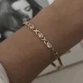 Elegante brazalete dorado fino con cristales ovales claros y eslabones en forma de X - Brazalete Torcido de Circonia (BR26Y0355)