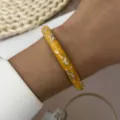 Close-up of a vintage yellow enamel bangle with gold floral patterns on a wrist. - Bright Yellow (887-7)