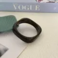 Gedetailleerd overzicht van onregelmatige bruine gemarmerde acryl armband met glans. - Donkerbruin