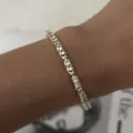 Primer plano de una delicada pulsera de tenis dorada con piedras blancas en la muñeca - Pulsera de Circonia Redonda con Nudo en X (BR26Y0355)