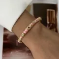 Detail shot of a gold-toned bangle with pink enamel flowers and crystals on a wrist. - Gold Pink White Enamel Petals (883-3)