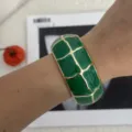 Nahaufnahme eines kräftig grünen Emaille-Armreifs mit goldenem Gittermuster am Handgelenk - Geometrisches Karo-Stil (3556) / Grün