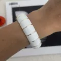 Detailansicht eines Manschettenarmbands mit weißer Emaille und goldfarbenen Streifen am Handgelenk. - Geometrisches Karo-Stil (2556) / Weißgold