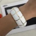 Detailansicht eines weißen Emaille-Armreifs mit goldenem Gittermuster am Handgelenk - Geometrisches Karo-Stil (3556) / Weißgold