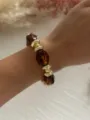 Dettaglio ravvicinato di un bracciale in acrilico retrò con perle tartarugate e metallo dorato - Caffè Trasparente e Oro
