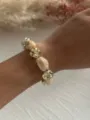Nahaufnahme eines Retro-Armbands aus Acrylmarmor und goldfarbenen Perlen am Handgelenk - Marmorweiß & Gold