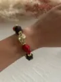Detailansicht eines Retro-Armbands mit unregelmäßigen Acrylperlen an einem Frauenhandgelenk. - Rot & Braun & Gold