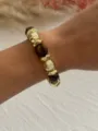 Nahaufnahme eines Vintage-Armbands mit goldenen Perlen und braunem Acryl-Detail. - Kaffee + Gold