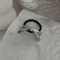 Detailaufnahme eines minimalistischen silbernen Haargummis auf weißer strukturierter Oberfläche - Gekreuzte Unregelmäßige Manschette (2025397) / Silber