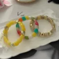 Set di braccialetti colorati in resina con perle dorate su un vassoio decorativo. - Set Sovrapposto / Set Contrasto Giallo Brillante (824-4)