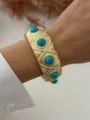 Detailed view of an ornate gold-tone alloy bangle featuring vibrant turquoise stones on a wrist - Wide Blue Turquoise Style (A656)