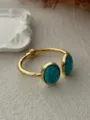 Detailed view of an elegant gold-toned bangle featuring dual oval turquoise stones - Open Oval Blue Turquoise Style (A656)