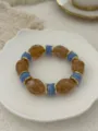 Vintage amber and blue marbled glass bead elastic bracelet displayed on white plate - Brown And Blue