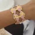 Eleganter breiter goldfarbener Armreif mit rosa Emaille-Schleifen und strukturierter Oberfläche - Rosa Schleifenstil