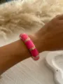Detail shot of a vibrant pink enamel bangle with gold accents on a model's wrist. - Curved Segment Style / Fuchsia Gold 157