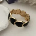 Dettaglio ravvicinato di un bracciale rigido dorato vintage con cuori in smalto nero. - Stile Cuore Nero e Oro (1583) / Oro