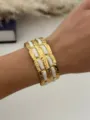 Luxuriöser vergoldeter Edelstahl-Armreif mit weißen Emaille-Einlagen am Handgelenk getragen - Gold Weiß Ziegelmuster