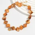 Detaillierte Ansicht einer unregelmäßigen Bernstein-Muschelkette auf weißem Ständer. - Halskette (1056640) / Orange