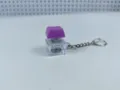 Mechanical keyboard switch keychain detail view showing clear housing and glowing purple cap. - 004