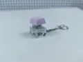 Close-up view of a transparent mechanical keyboard switch keychain with a purple keycap. - 013