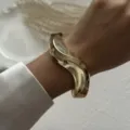 Detailed view of a stylish gold irregular wave bangle worn on a wrist with silk sleeve - Irregular Wave Hollow Cuff