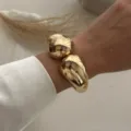 Primo piano di un bracciale rigido dorato lucido con doppio design a goccia al polso - Stile a Doppia Goccia d'Acqua (213) / Oro