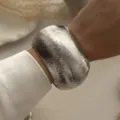 Detailaufnahme eines breiten, texturierten silbernen Metallarmreifs mit elegantem weißen Satinärmel - Breiter Gestreifter Gebogener Armreif (217) / Silber