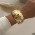 Dettaglio di un ampio bracciale a polsino in oro martellato indossato al polso chic - Stile Martellato (213) / Oro