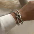 Elegante Nahaufnahme eines klobigen silbernen Metallarmbands mit Knotendesign am Handgelenk. - Knoten Design Kreuz Armreif (217) / Silber