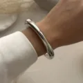 Detailansicht eines klobigen silbernen geschwungenen Metallarmreifs mit weißem Seidenärmel - Minimalistischer Stromlinienförmiger Offener Armreif (217) / Silber