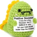 Cute crochet green dinosaur plush toy holding a positive quote card for emotional support. - Dinosaur