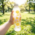 Hand holding a frosted water bottle with yellow flower patterns in a sunlit park. - 1000ml / Yellow Floral (Silver Cap)