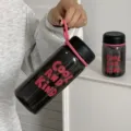 Main tenant une bouteille d'eau translucide avec bord et dragonne roses - Noir Cool 550ml