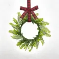 Macro view of lush green Persian leaf wreath with a rustic red buffalo plaid bow. - Red and Black Buffalo Plaid Bow Style