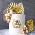 Detail view of champagne gold cake topper balls and palm leaves, elegant birthday decor. - Platinum Ginkgo Leaves