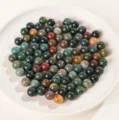 Assortimento di perle tonde in agata indiana naturale senza foro su un piatto bianco - 8mm / Perla di Agata Indiana Naturale Senza Foro