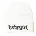 Nahaufnahme der schwarzen 'babygirl' Stickerei auf einer weißen gestrickten Beanie-Mütze - Weiß